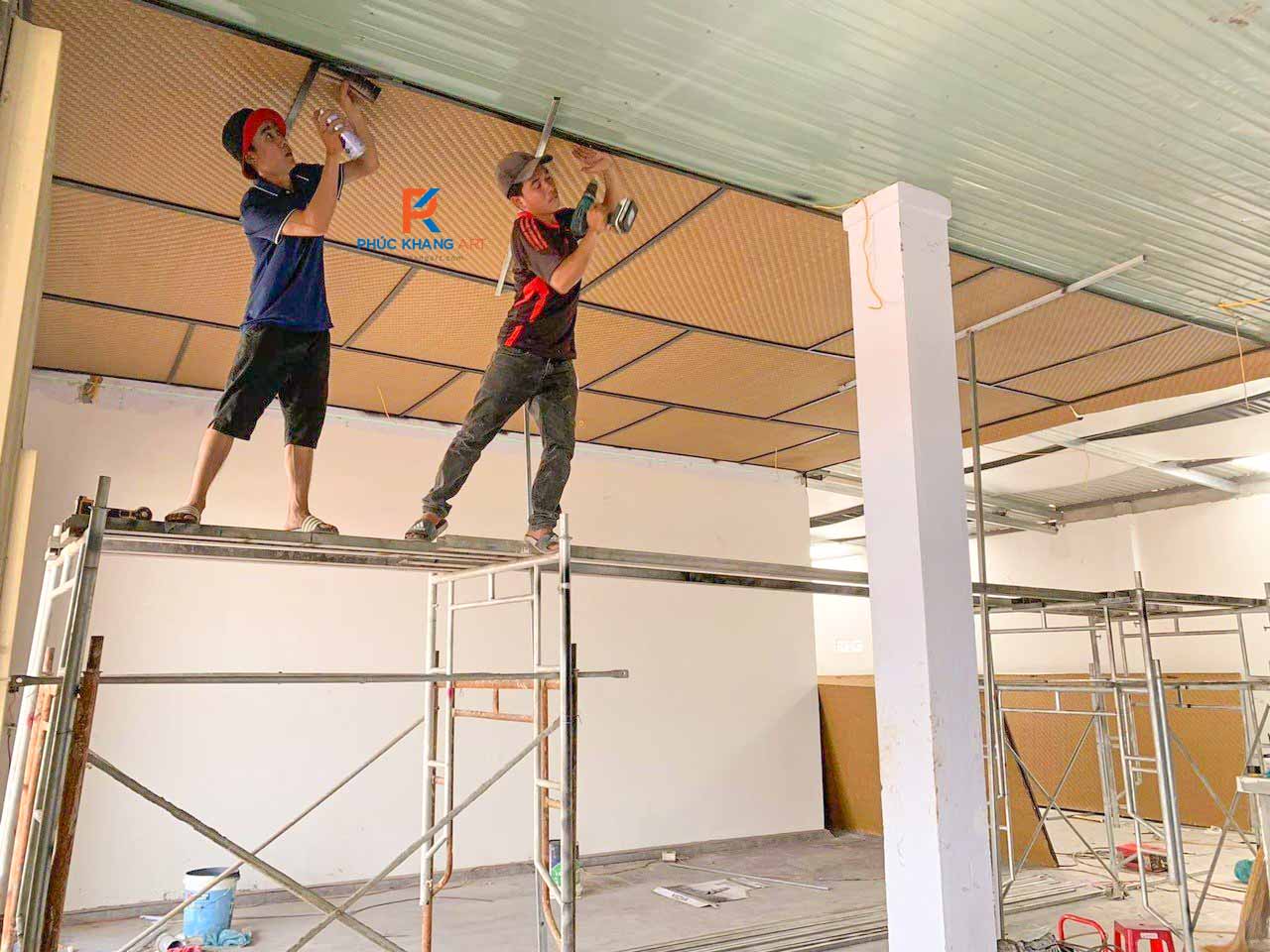 Thi Công Trần Cót ép Nhân Tạo - Báo Giá Chi Tiết 2025 7 Hai thợ đang thi công trần bằng cót ép nhân tạo trong không gian nhà hàng lớn.