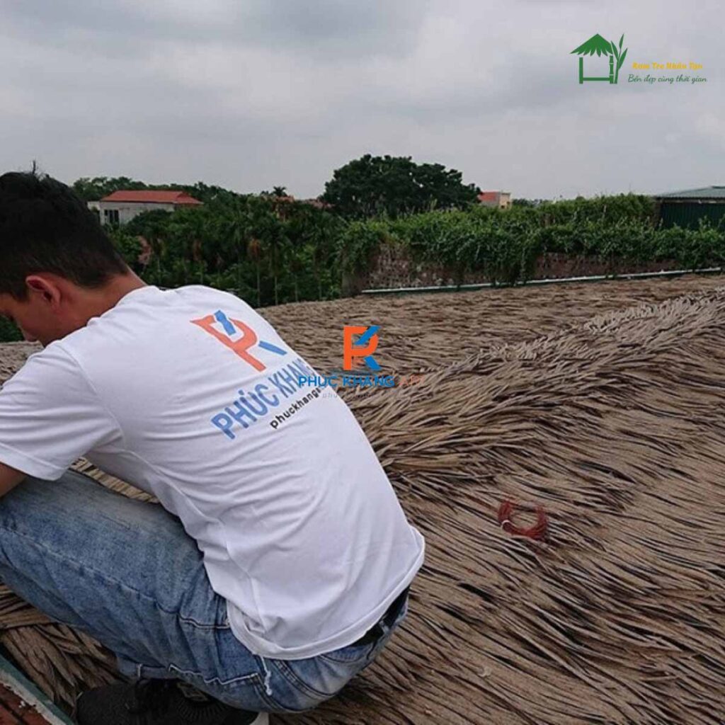 Thợ thi công hoàn thiện phần đỉnh mái bằng tấm rơm nhân tạo chuyên dụng