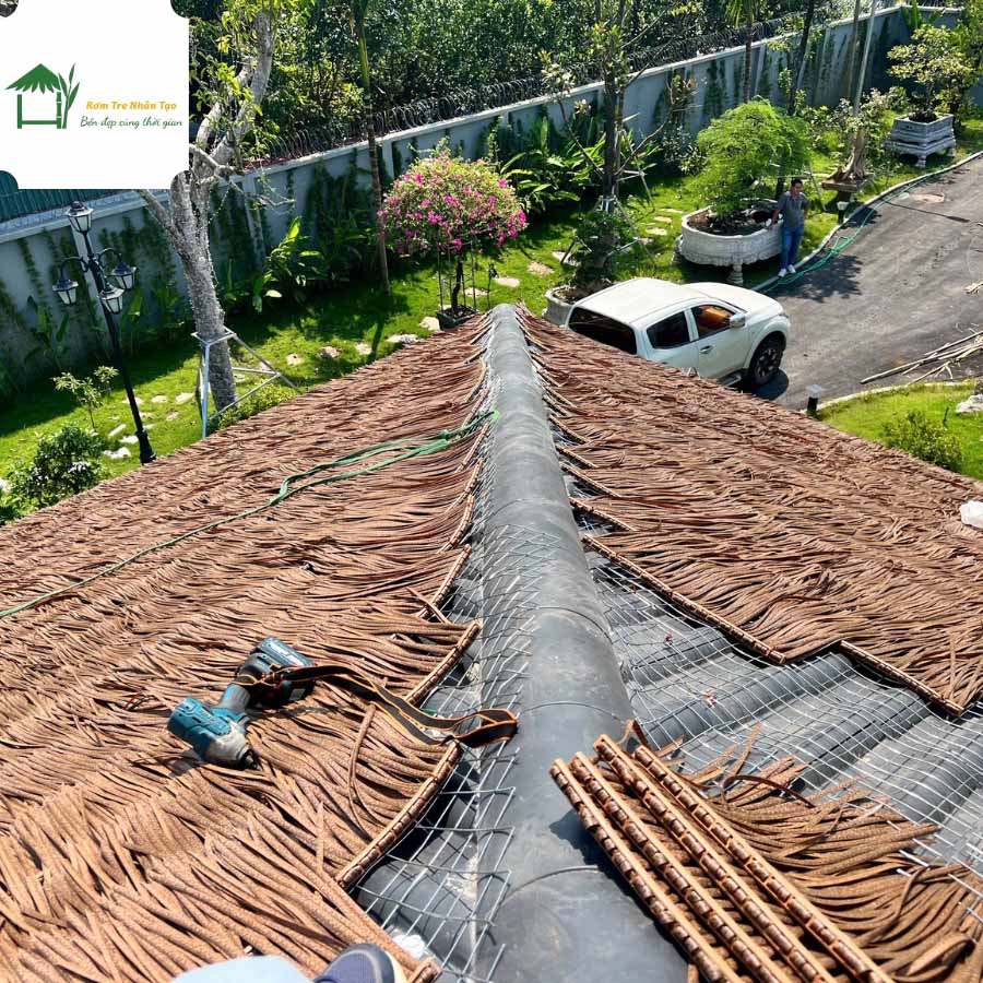 Thi công rơm nhân tạo trên mái tôn với lớp rơm chồng đều, có khung lưới và đỉnh mái được bọc chống dột.