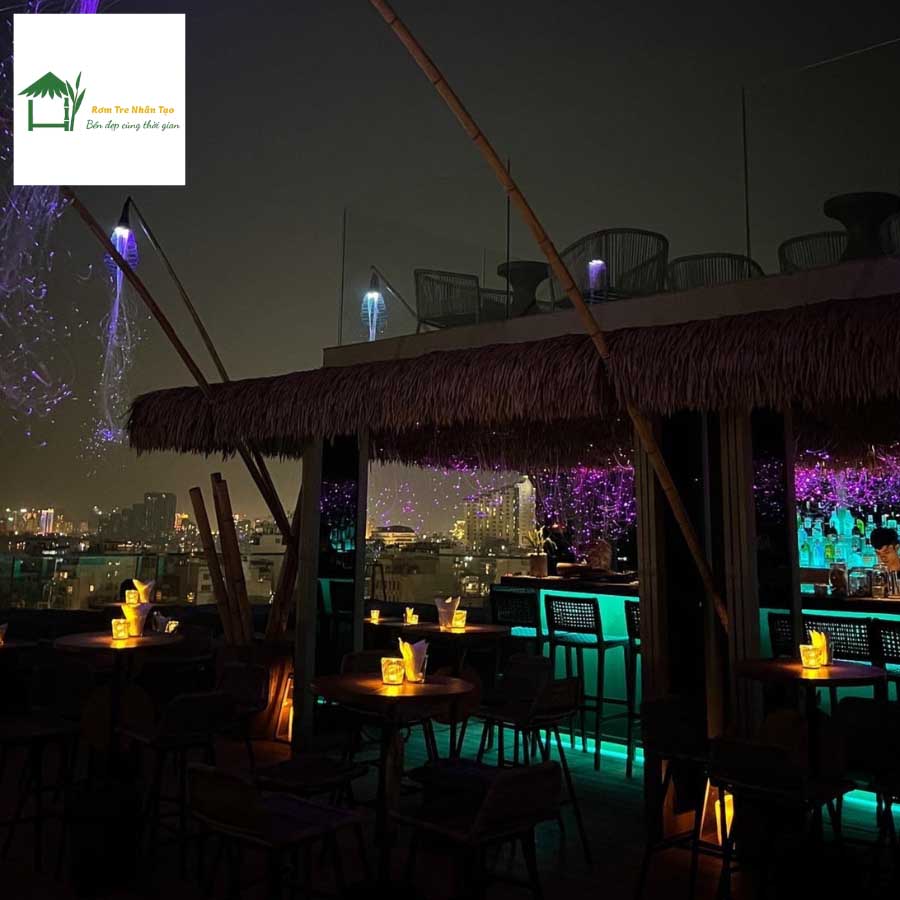 Quầy bar ngoài trời ban đêm, mái rơm nhân tạo, ánh sáng đèn neon nhiều màu.